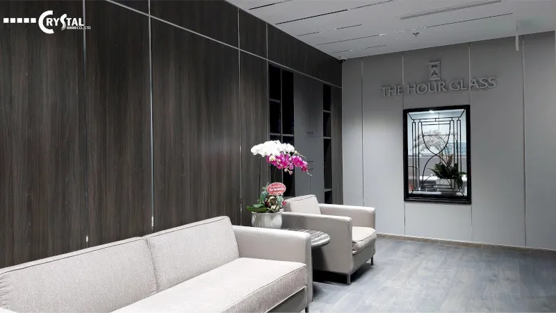 Khu vực tiếp khách với sofa xám, bàn kính và vách gỗ tối màu tại văn phòng SGI